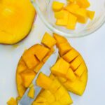 Removing cut mango with a knife.