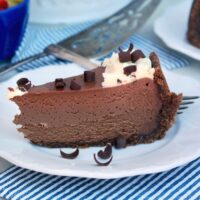 Slice of keto chocolate cheesecake on a white plate with a blue and white stripped napkin