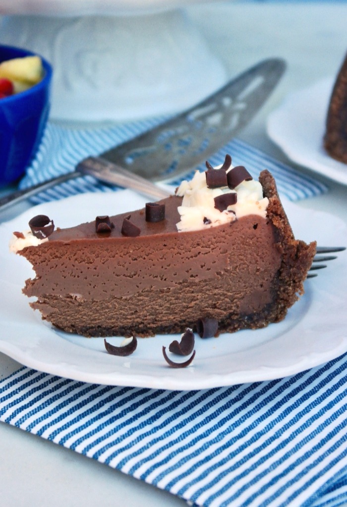 Slice of keto chocolate cheesecake on a white plate with a blue and white stripped napkin