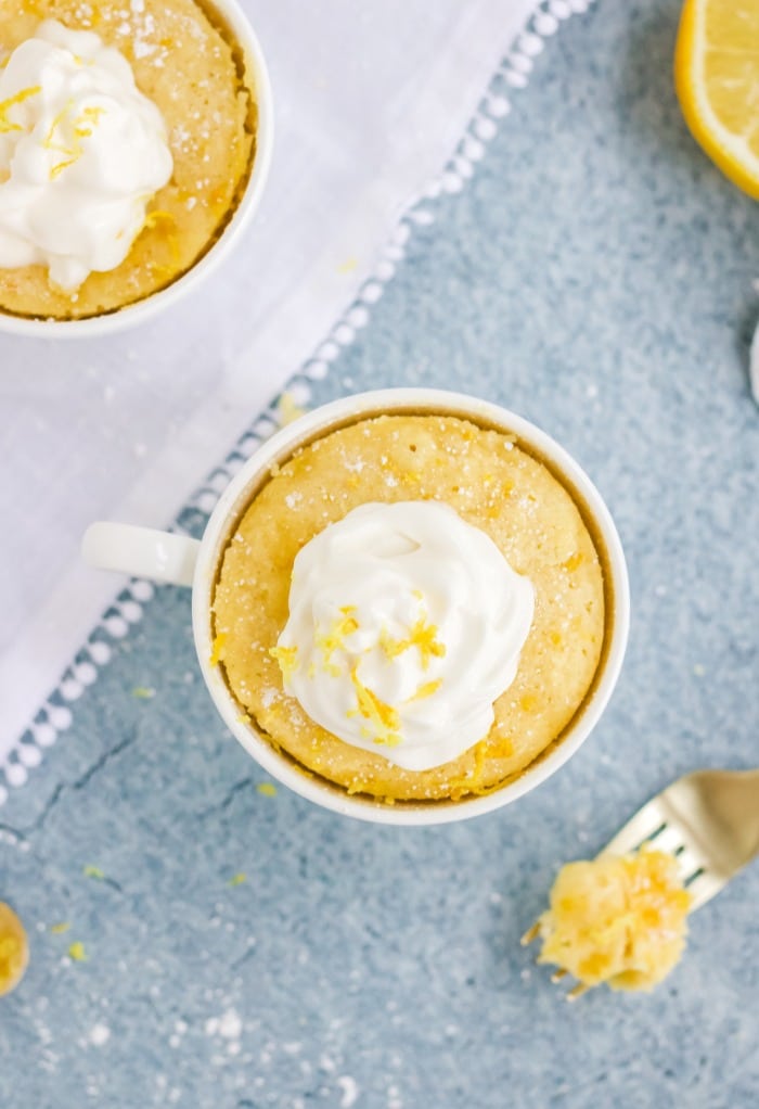 Overhead view of keto lemon mug cakes topped with whipped cream and a sprinkle of lemon zest.