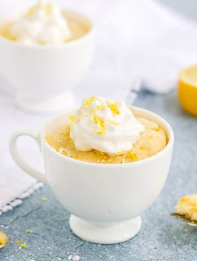Keto lemon mug cake in a white mug topped with whipped cream.