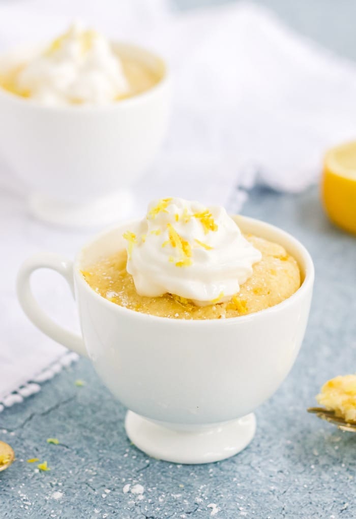 Keto lemon mug cake in a white mug topped with whipped cream.