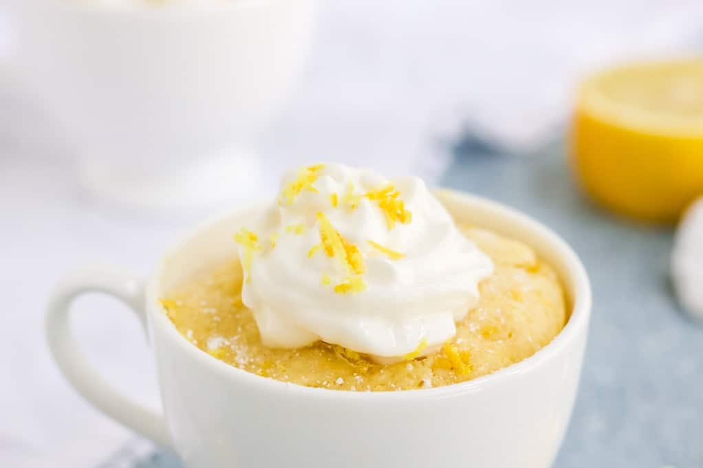 Close up view of keto lemon mug cake in a white mug topped with fresh whipped cream. 