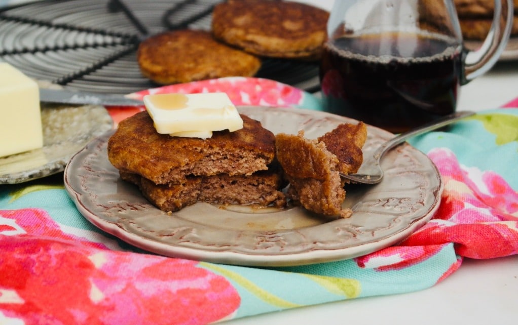 horizontal view of low carb pancakes topped with butter and maple syrup on a tan plate. 