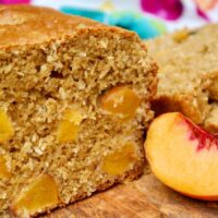 Homemade peach bread with a slice of fresh peach on the side.