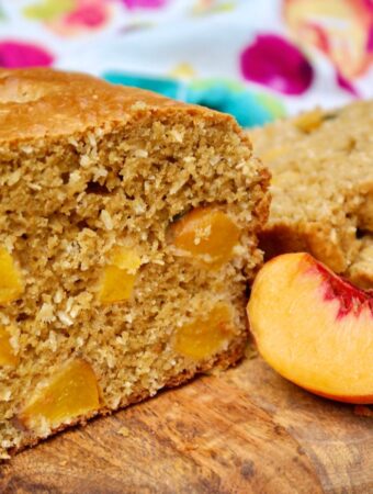 Homemade peach bread with a slice of fresh peach on the side.