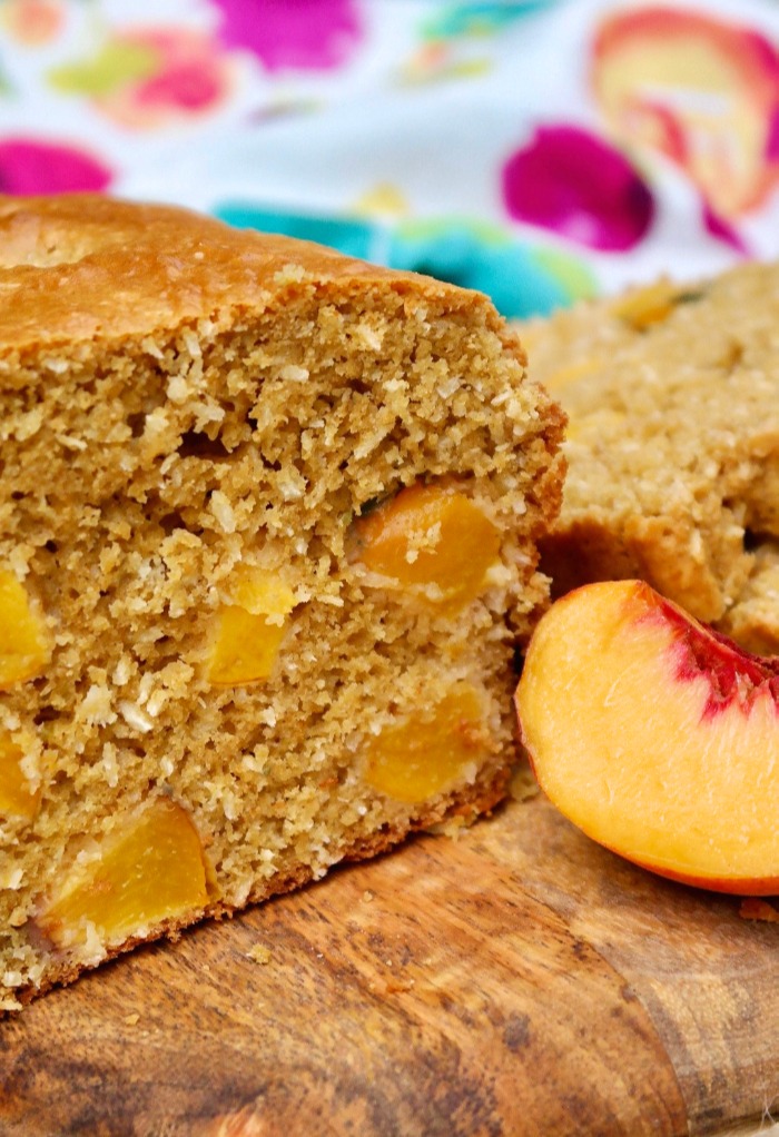 Homemade peach bread with a slice of fresh peach on the side.