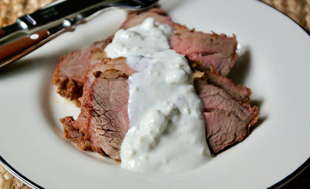 A white plate with steak topped with a white cheese sauce. 