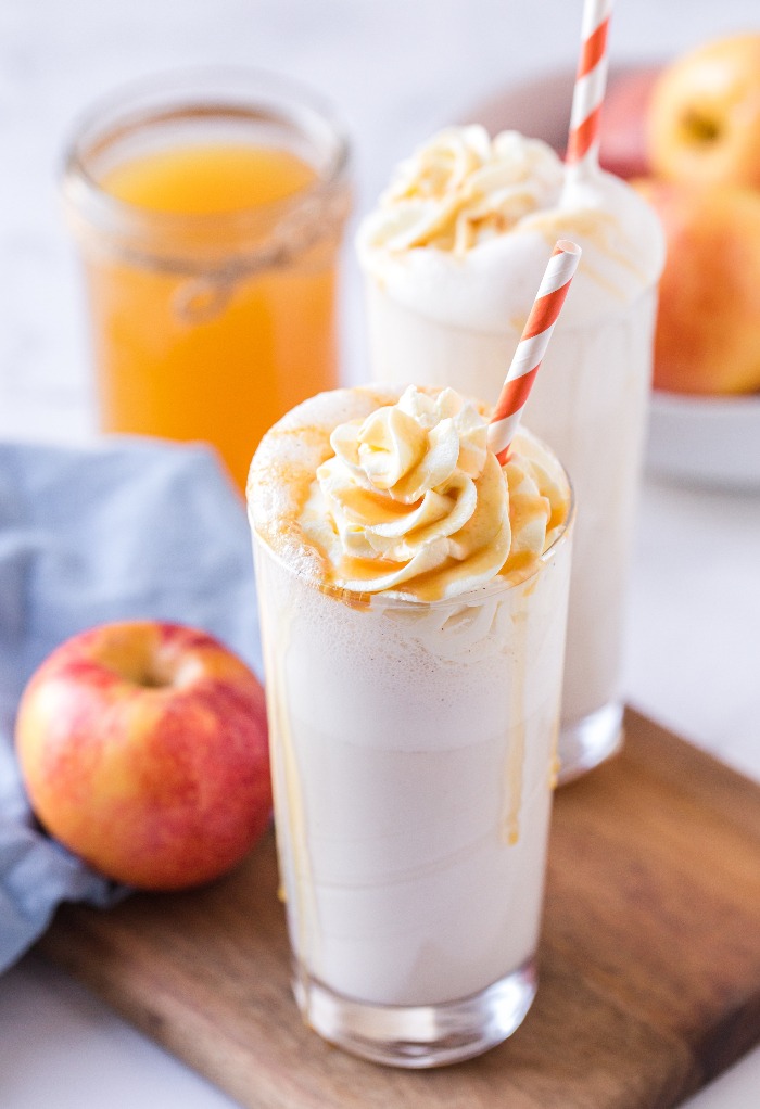 Two clear glasses filled with vanilla milkshake on a brown board. 