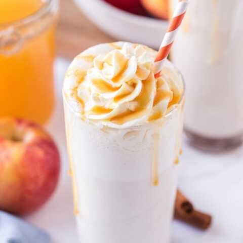 Homemade apple milkshake in a clear glass topped with whipped cream.