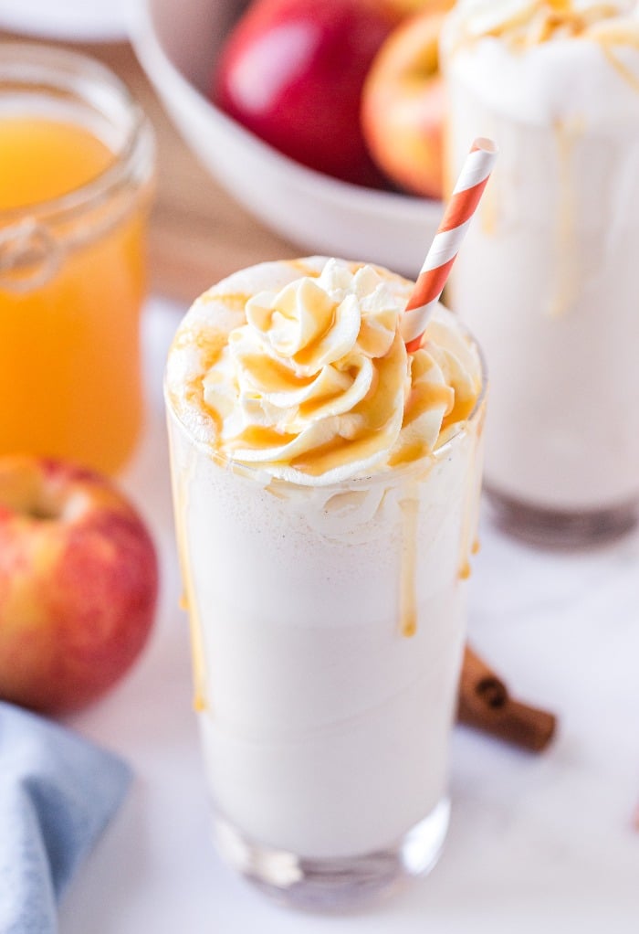 Homemade apple milkshake in a clear glass topped with whipped cream.