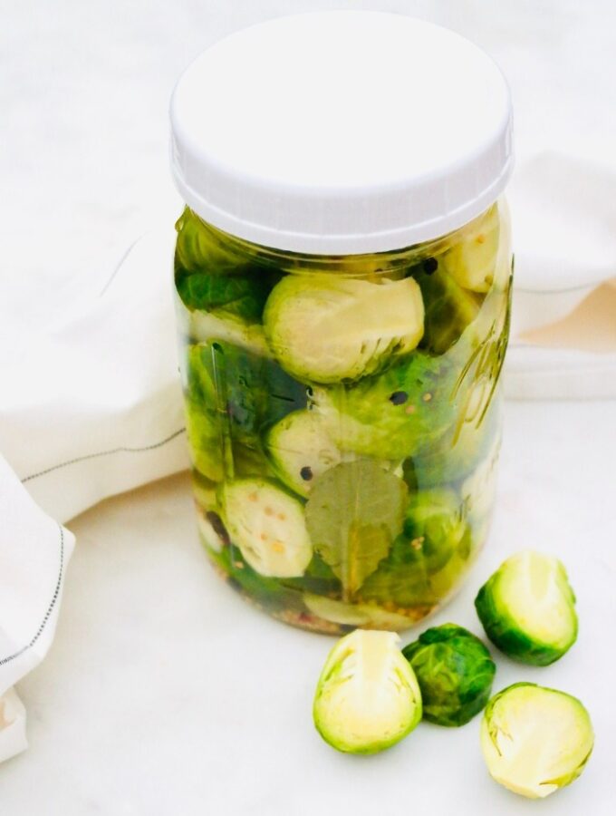 A mason jar filled with steamed brussels sprouts in a pickled vinegar mix.