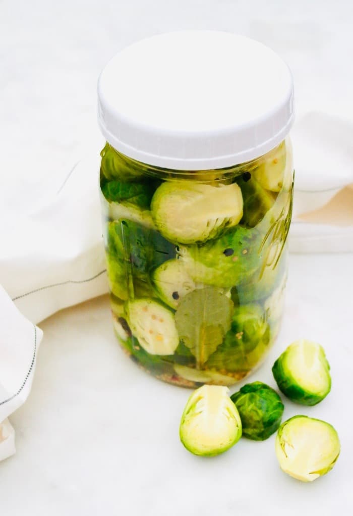 A mason jar filled with steamed brussels sprouts in a pickled vinegar mix.