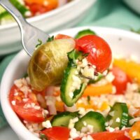 A forkful of cauliflower rice salad from a white bowl.