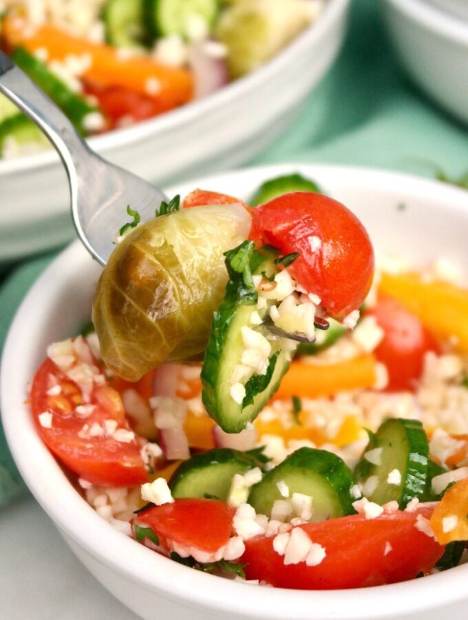 A forkful of cauliflower rice salad from a white bowl.