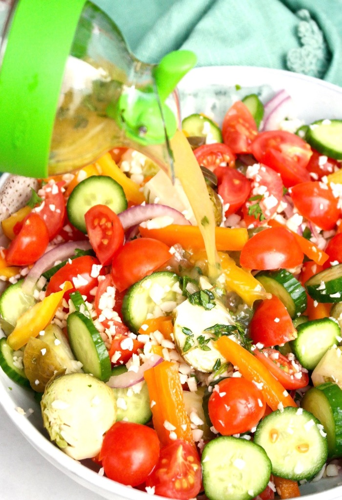 Pouring Greek dressing a bowl filled with vegetables. 