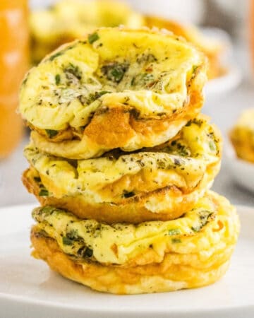Egg muffins cooked in a muffin tin stacked on a white serving dish.