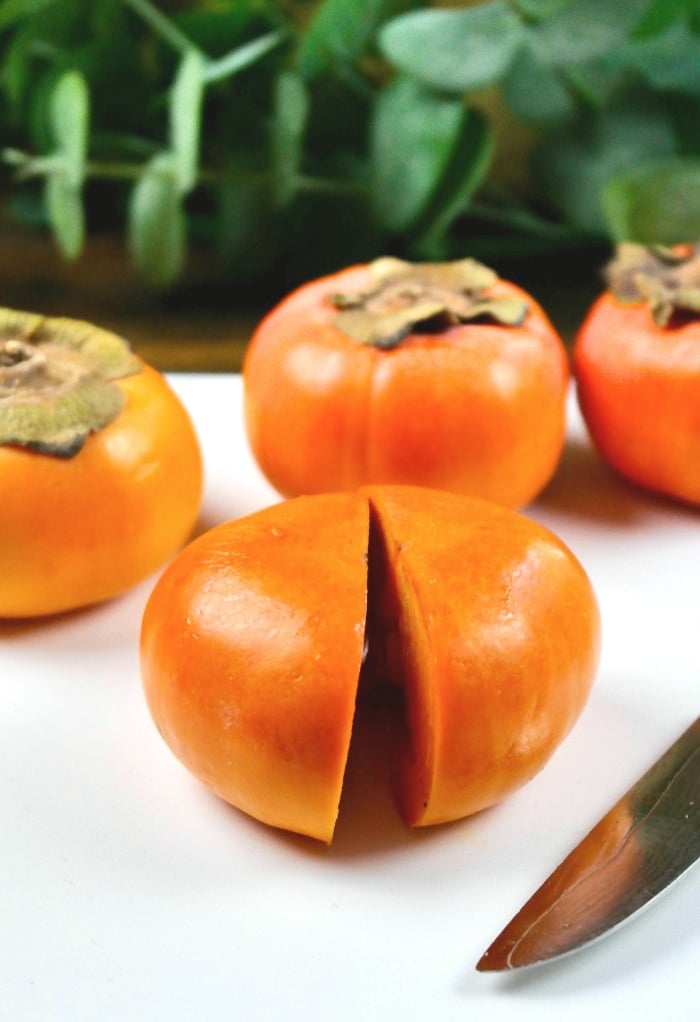 Slice the persimmon in half on a white cutting board. 