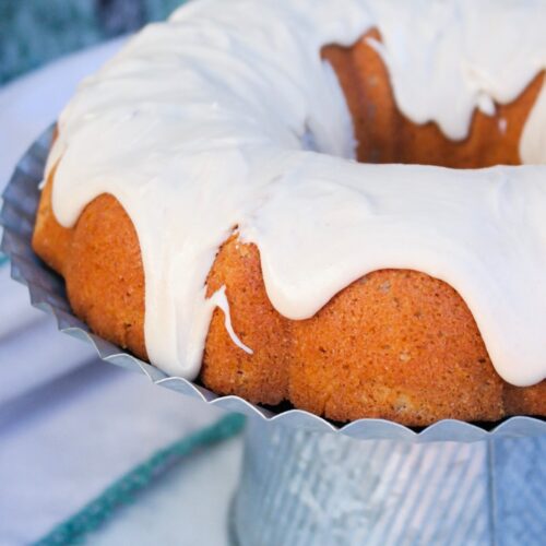 Spice cake bundt cake topped with browned sugar icing on an aluminum cake plate.