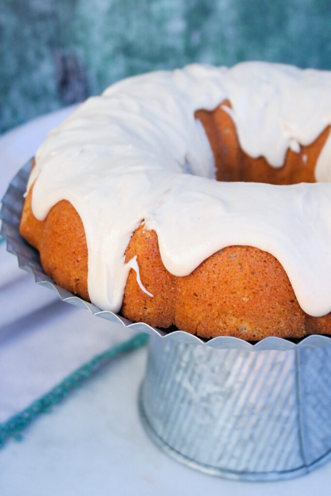 Spice cake bundt cake topped with browned sugar icing on an aluminum cake plate.