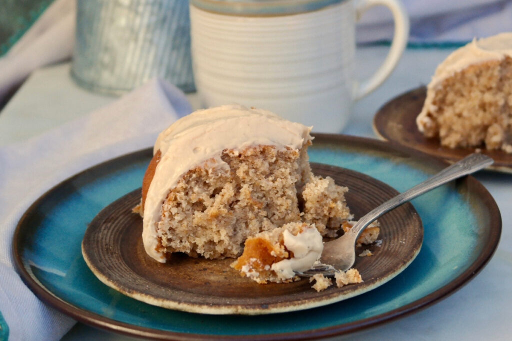 A landscape view of a slice of spice cake with a cup of coffee on the back of the plate.