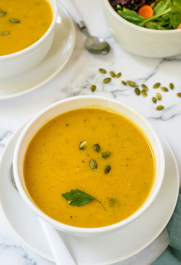 Fresh butternut squash soup in a white bowl with a green salad on the side. 