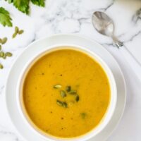 A white bowl filled with butternut squash soup topped with pumpkin seeds.