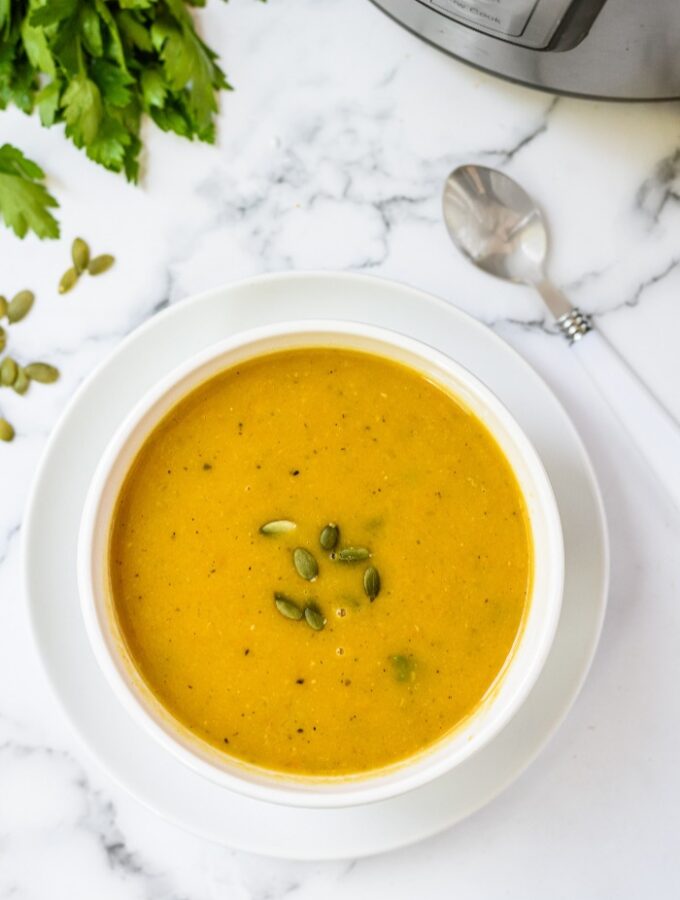 A white bowl filled with butternut squash soup topped with pumpkin seeds.