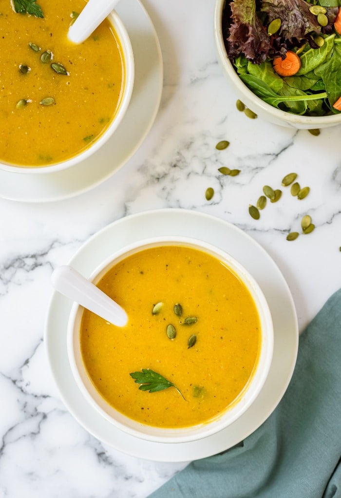 White bowls of butternut squash soup topped with pumpkin seeds. 