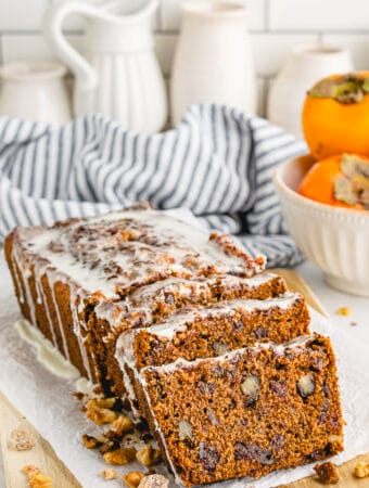 Sliced persimmon bread with nuts and topped with a glaze on a cutting board.