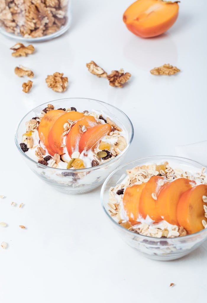 slices of persimmon on top of yogurt with granola in a clear bowl. 