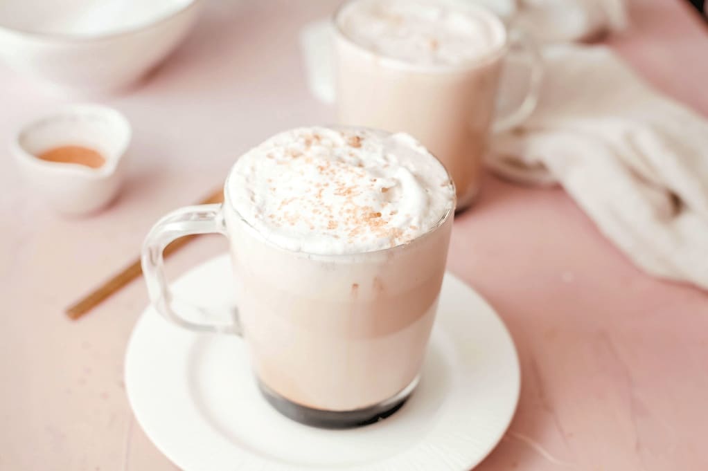 Two clear coffee mugs filled with coffee and topped with whipped cream.