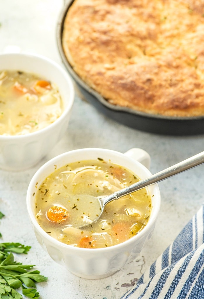 A white mug full of chicken soup with skillet bread on the side ready to eat. 