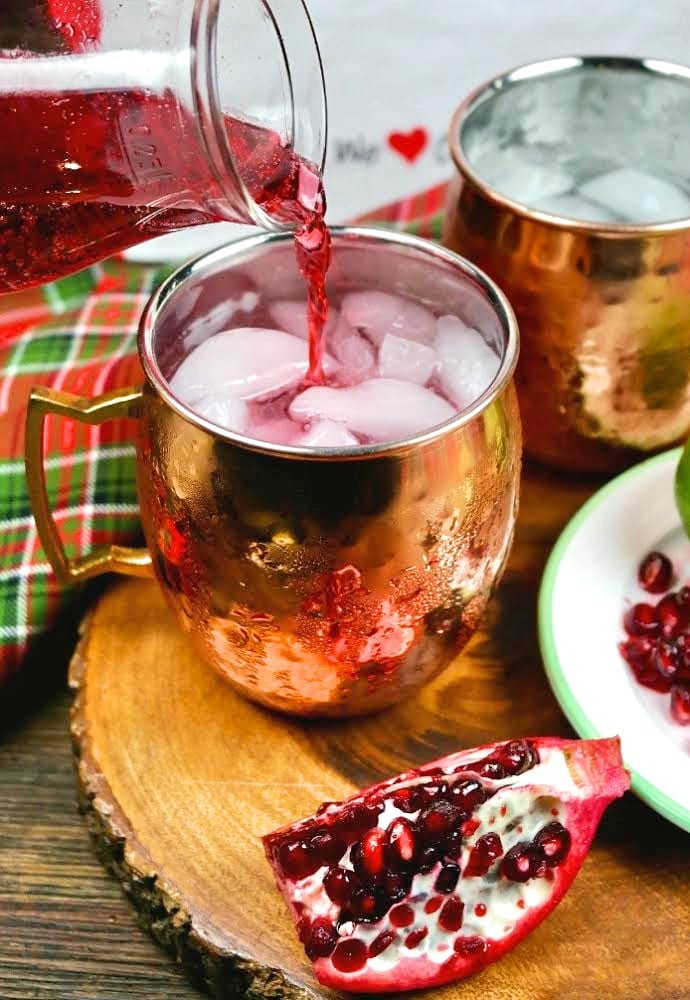 Pouring pomegranate juice into a copper mug to make a Moscow mule cocktail.