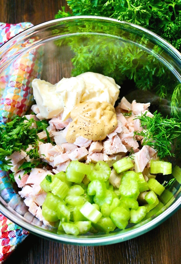 All the ingredients to make turkey salad in a clear mixing bowl ready to stir together.