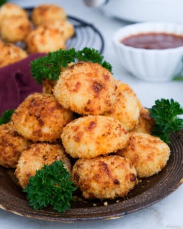 Stacked potato balls on a brown serving plate with parsley ready to eat.