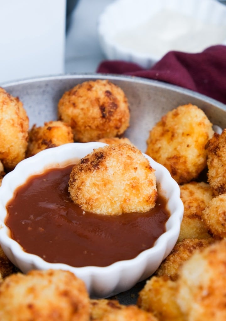 Mashed potato balls cooked in an air fryer on a stainless steel bowl with ketchup dip. 