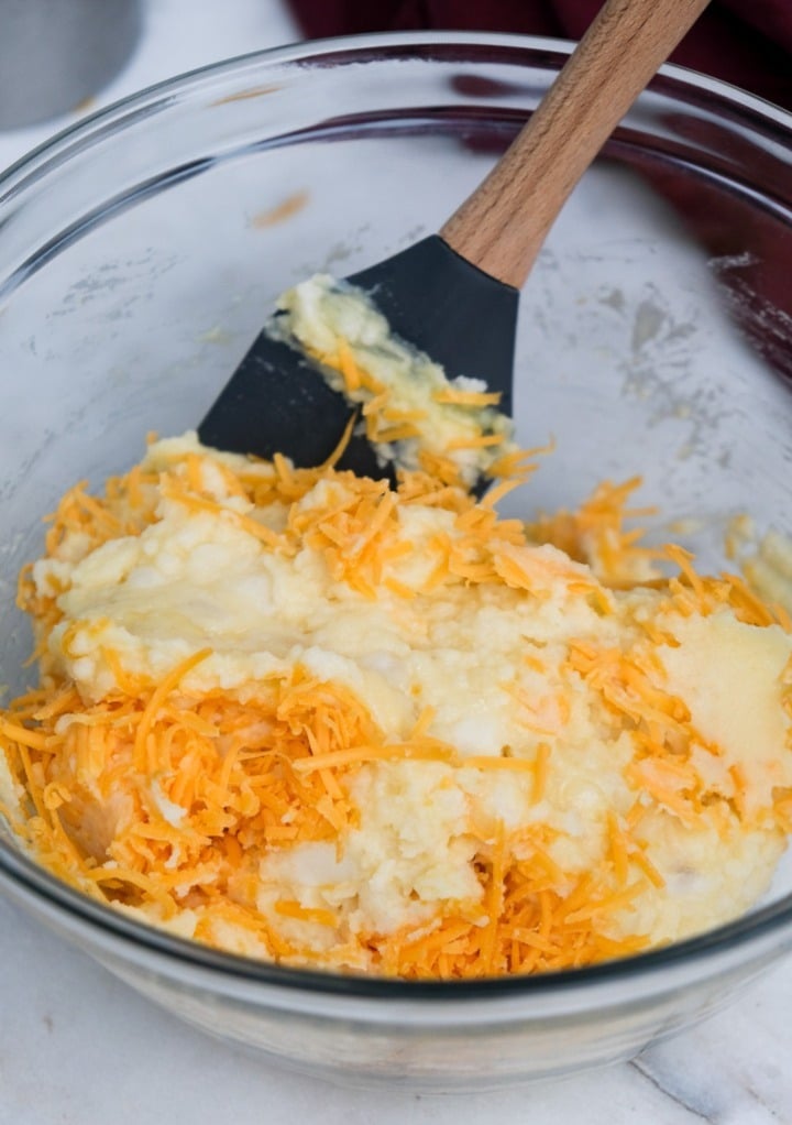 Mashed potatoes in a clear mixing bowl with cheddar cheese. 