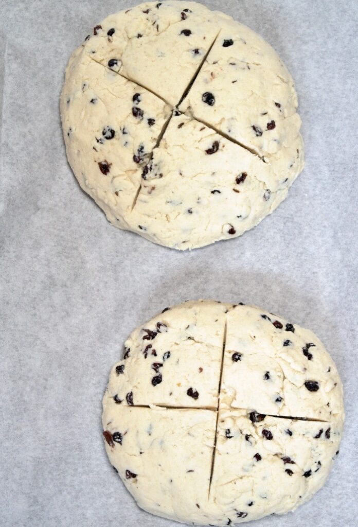 Unbaked soda bread on a baking sheet topped with white parchment paper ready to be put in the oven. 