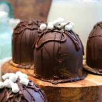 Keto hot chocolate with sugar free chocolate bombs on a wood serving tray with milk in the background.