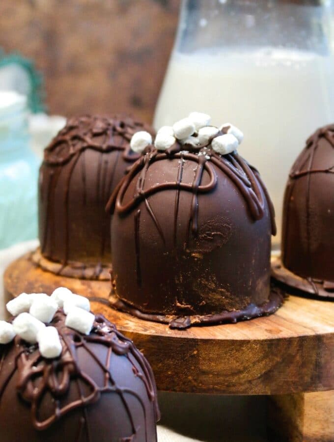 Keto hot chocolate with sugar free chocolate bombs on a wood serving tray with milk in the background.