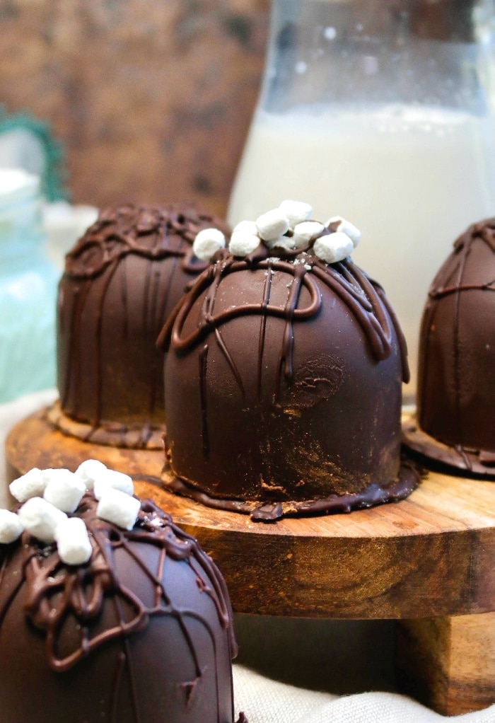 Keto hot chocolate with sugar free chocolate bombs on a wood serving tray with milk in the background. 