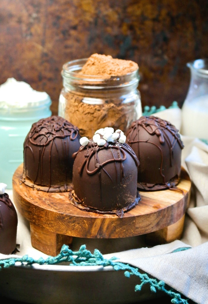 The finished hot chocolate bombs on a wooden stand with cocoa in the background ready to use. 