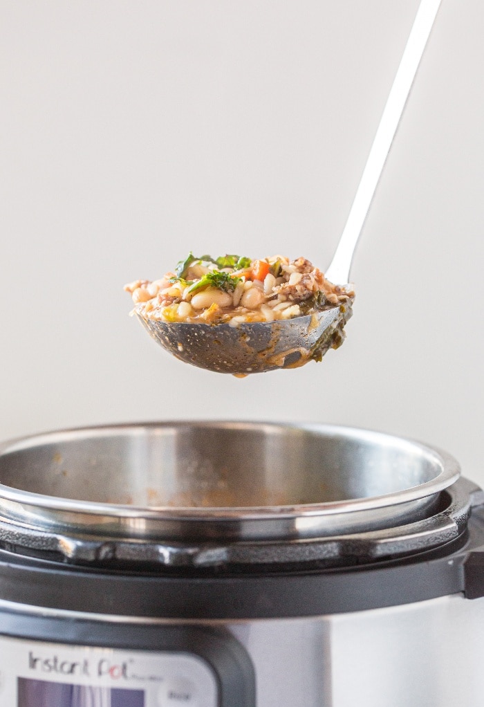 A ladle full of Italian sausage soup ready to be put in a bowl for serving. 