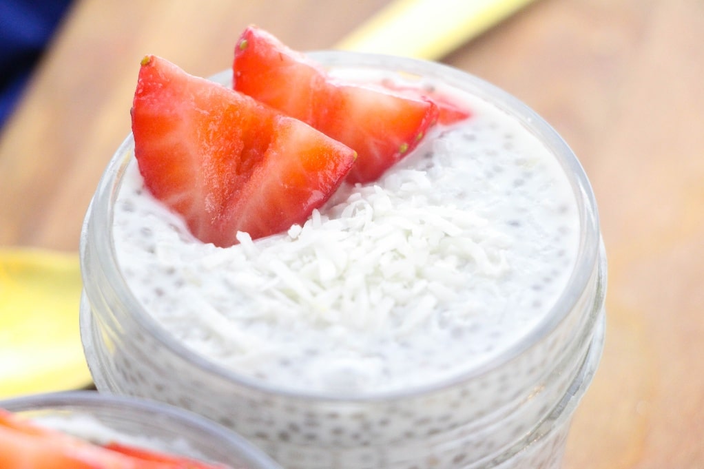 A horizontal view of the top of chia pudding in a clear jar with a fresh diced strawberry on top. 