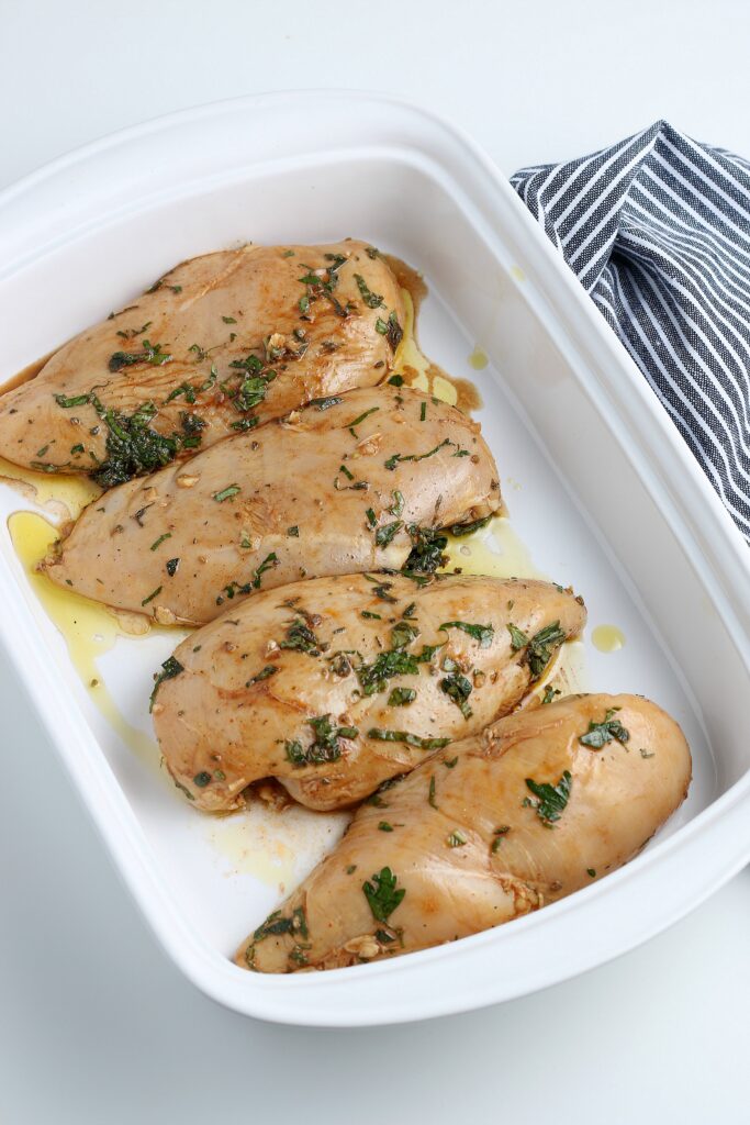 Marinated chicken in a white baking pan ready to be cooked in the oven. 
