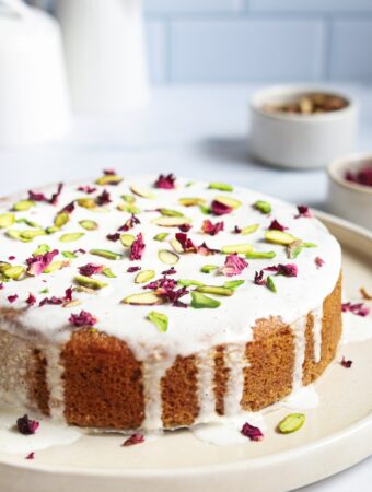 Homemade cake with a white icing topped with rose petals on a serving plate