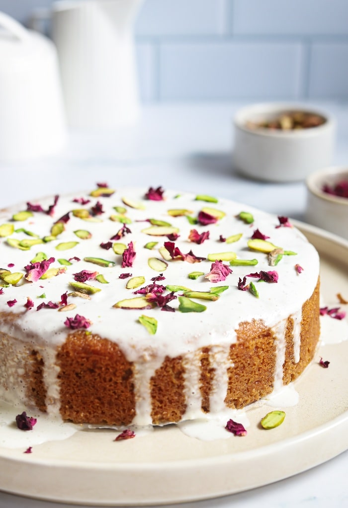 Homemade cake with a white icing topped with rose petals on a serving plate
