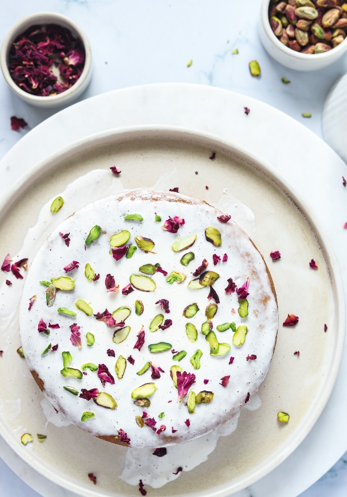 Top view of a rose and pistachio decorated cake on a white serving plate.  