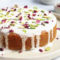 Decorated Persian love cake topped with rose petals and pistachios on a cream serving cake plate.